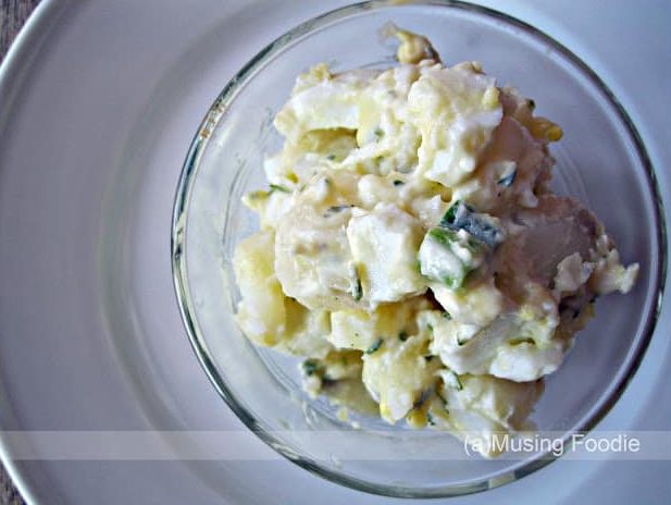 Creamy potato salad with egg and fresh herbs in a clear glass bowl.