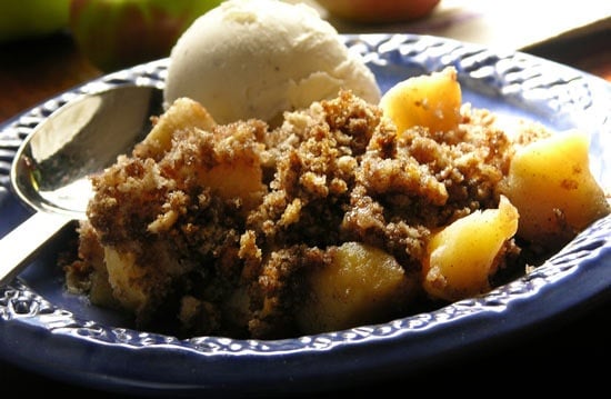 Delicious apple crisp topped with creamy vanilla ice cream on a vibrant blue plate.