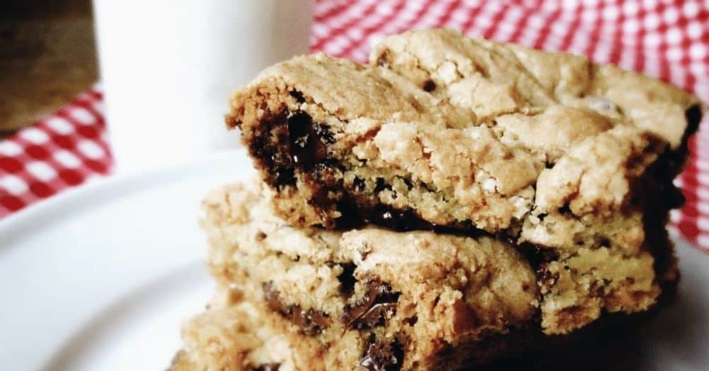 Stack of chocolate chip cookie bars with a glass of milk