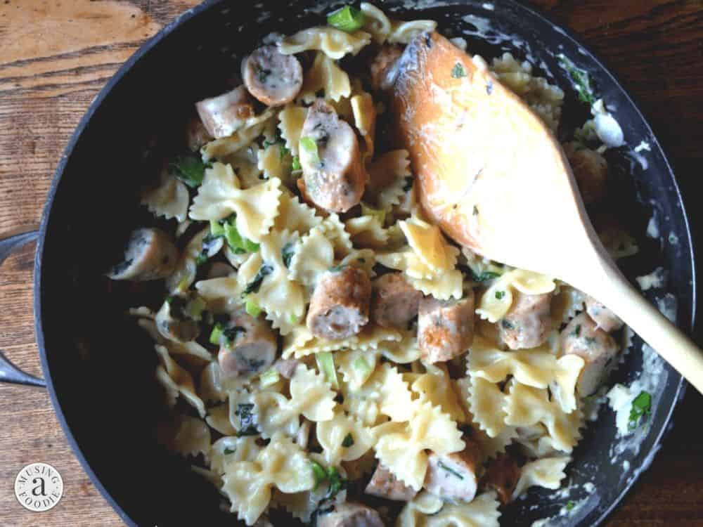 Skillet with faralle pasta cooked in a garlic cream sauce and served with seared chicken sausage.