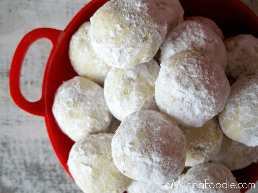 Almond lime snowball cookies dusted in powdered sugar in a vibrant red bowl.
