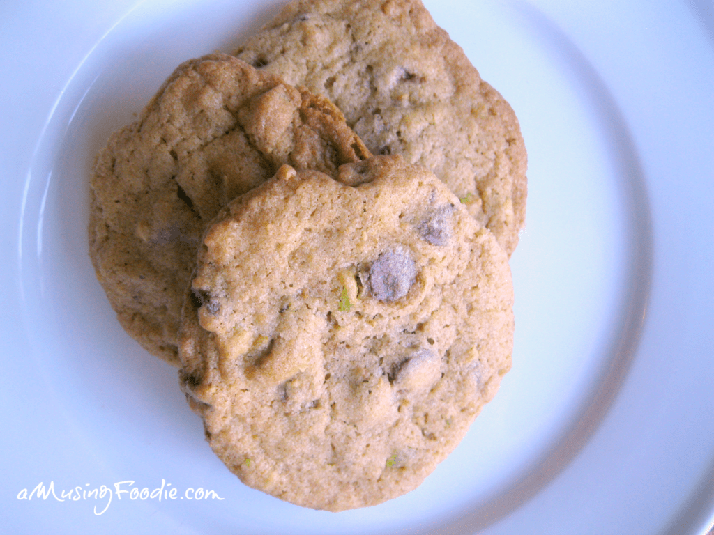 Freshly baked chocolate chip cookies with nuts on a simple white plate.