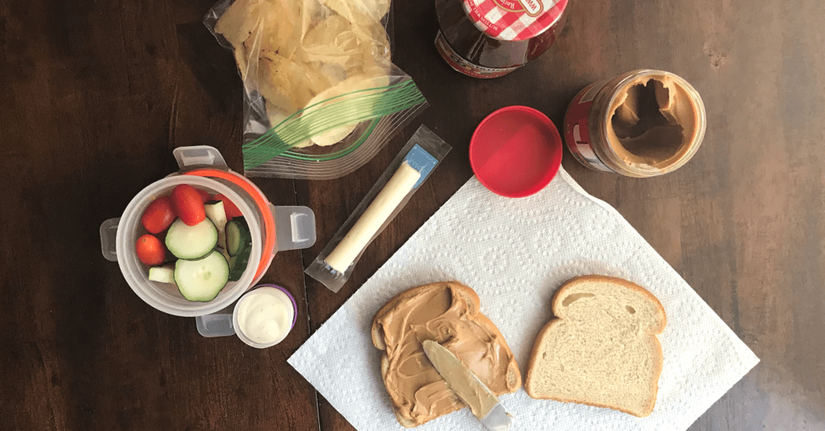 Peanut butter and jelly sandwich with fresh veggies and cheese on a wooden table.