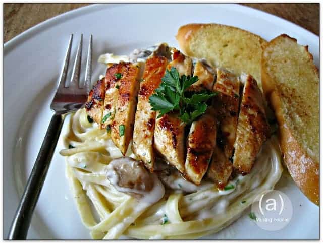 Delicious fettuccine alfredo topped with grilled chicken and served with garlic bread.