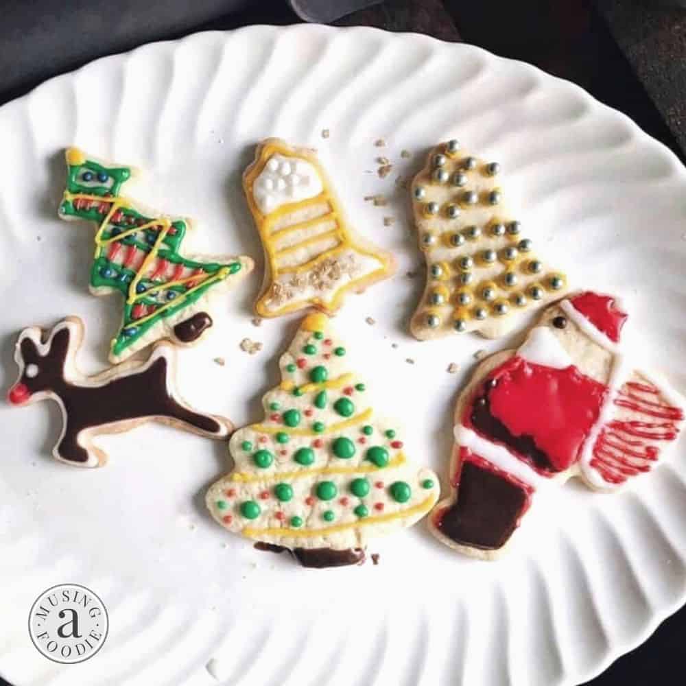 Colorful Christmas cookies in festive designs arranged on a decorative white plate.