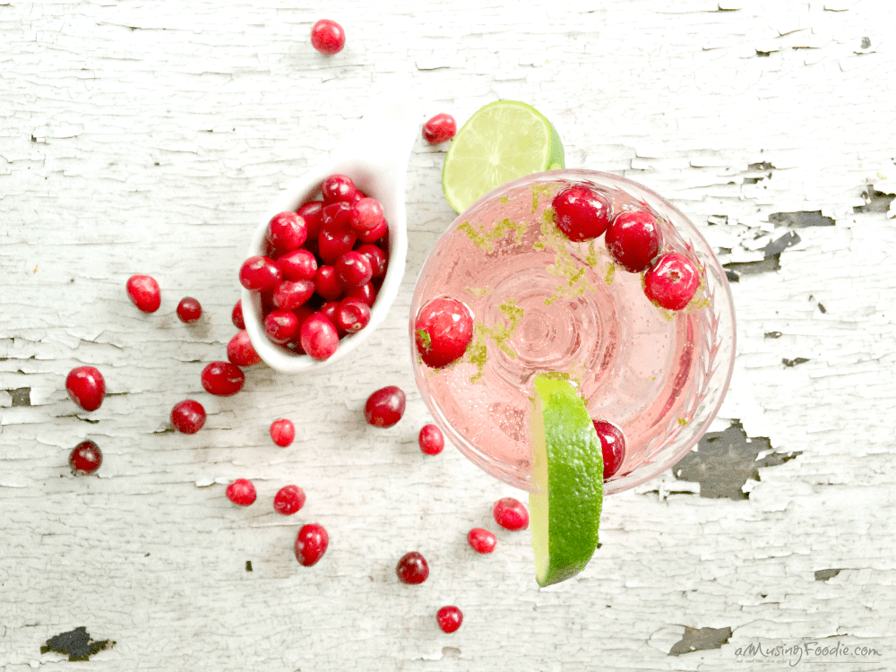 Refreshing pink cranberry lime cocktail with vibrant garnishes on rustic wood background.