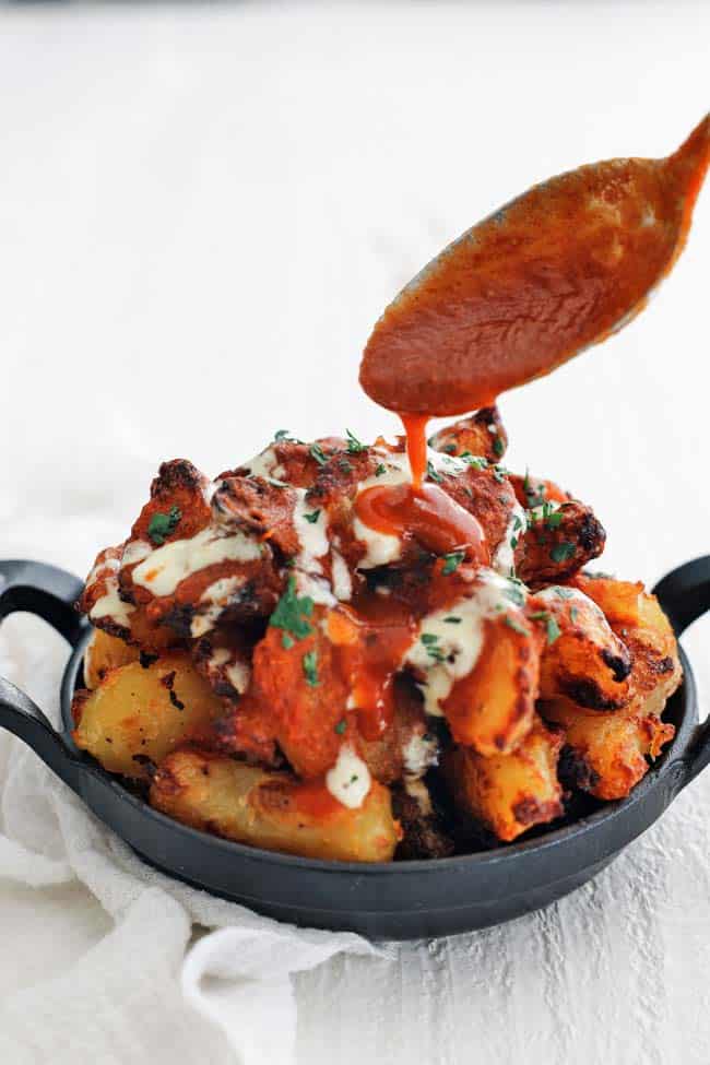 Patatas Bravas being topped with a rich red sauce from a spoon