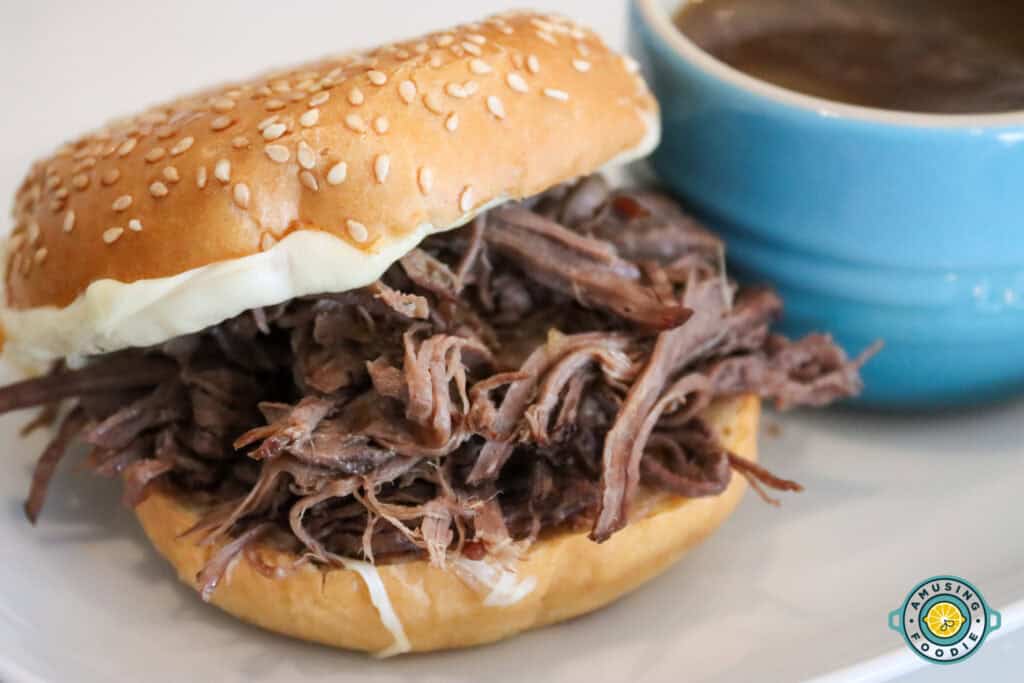 Shredded beef sandwich next to au jus dip