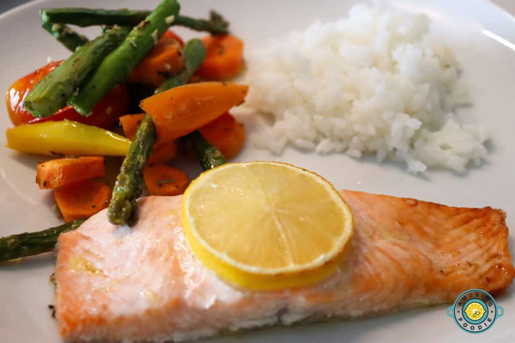 Salmon with sliced lemon on top with veggies and rice as sides